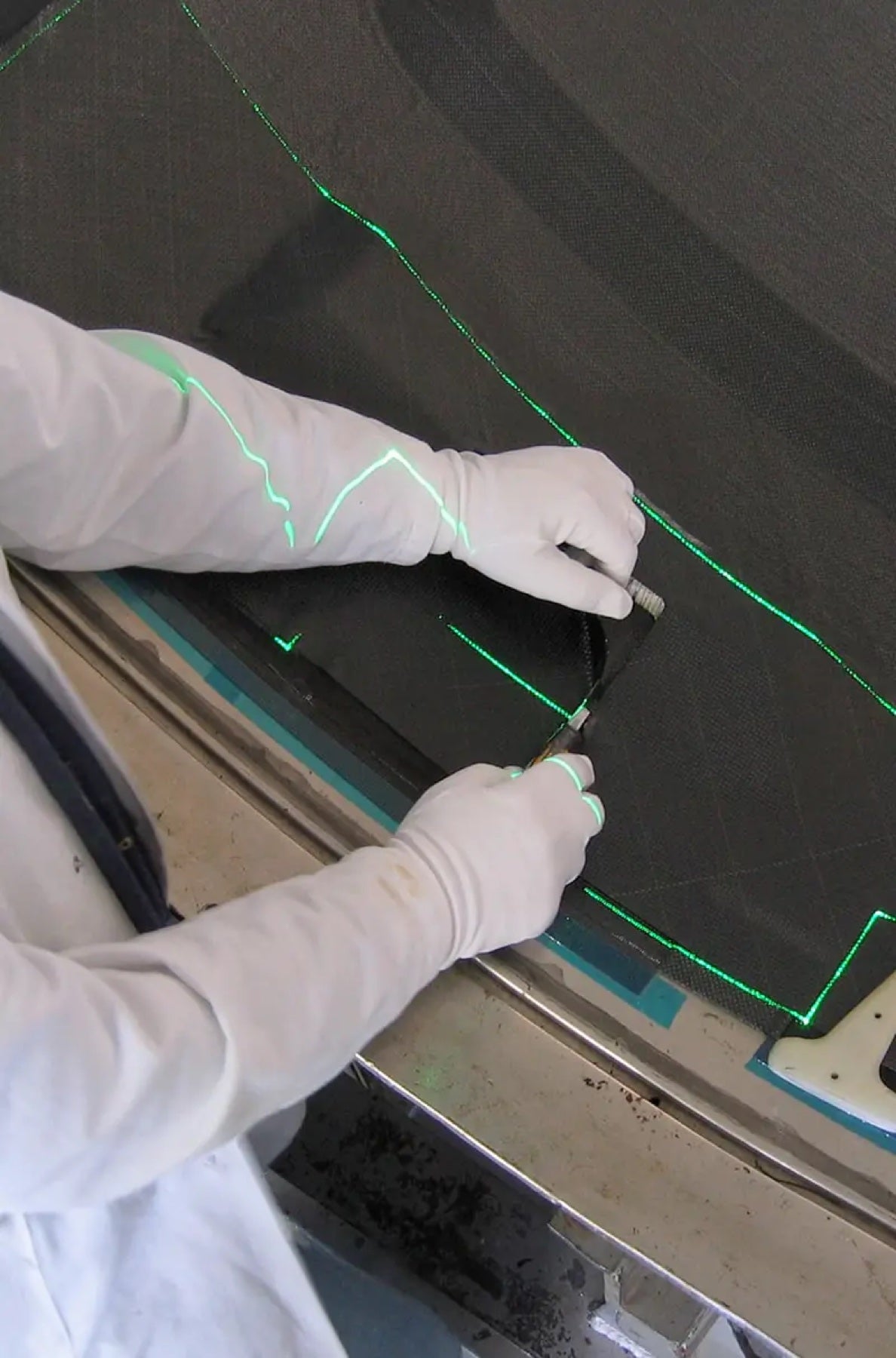 Gloved hands trimming composite material along a green laser-projected cutting line