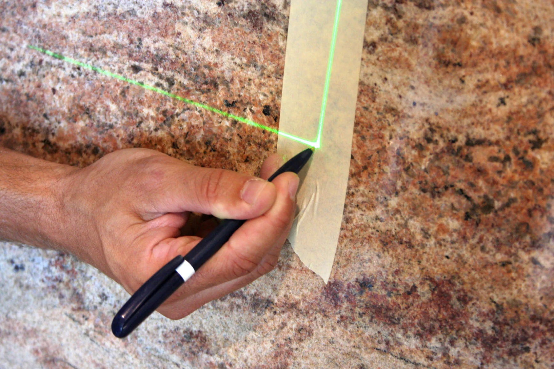 A green laser line marking a precise template edge on stone