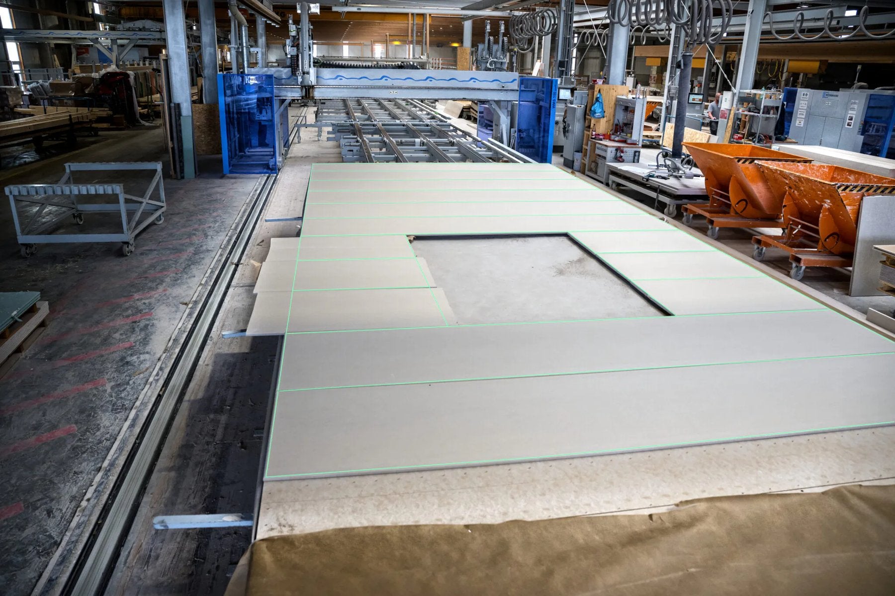 Green laser lines projected onto a large prefabricated panel on a factory line, marking every board edge and the cut-out