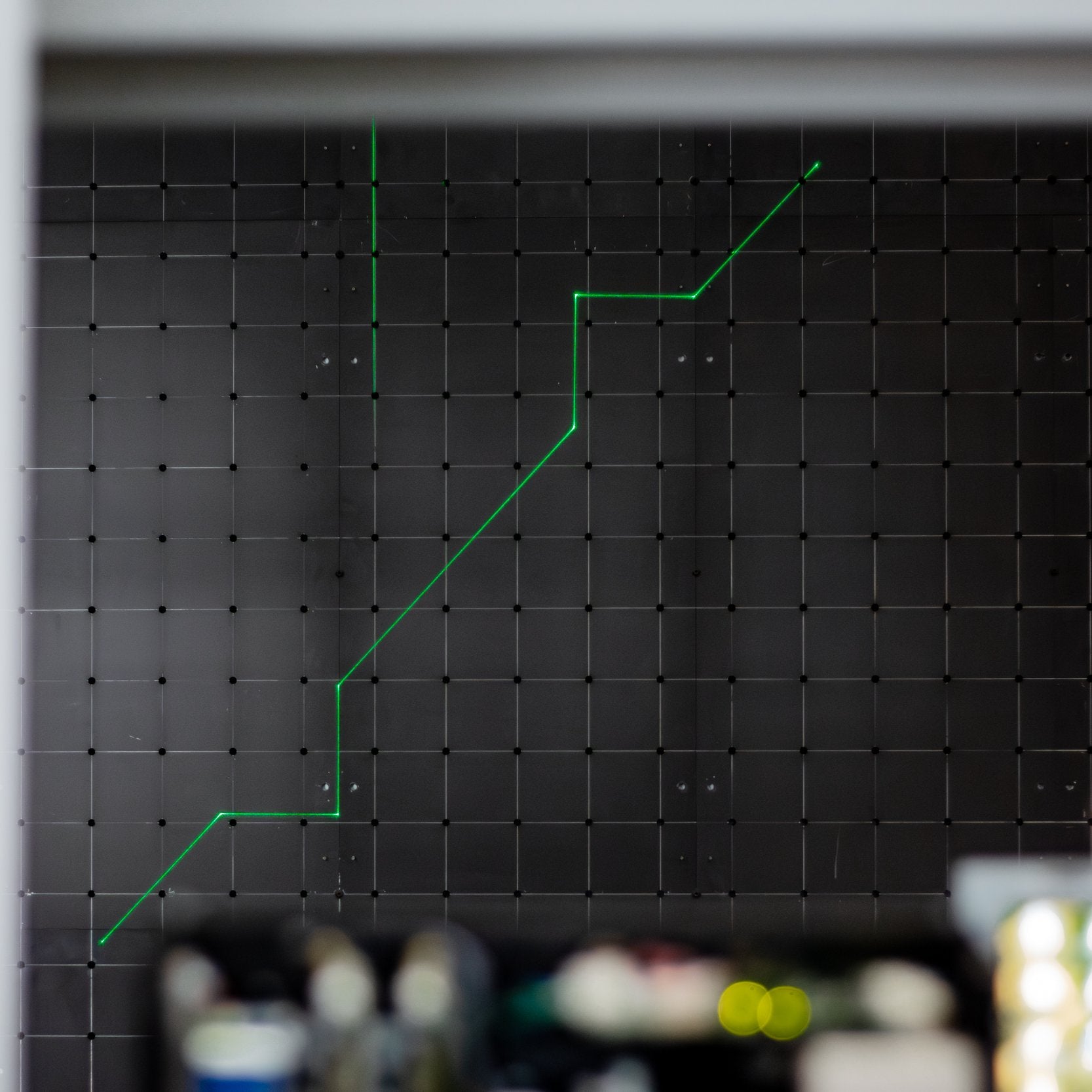 A green laser line projected across a perforated pin board, tracing a harness routing path between fixing points