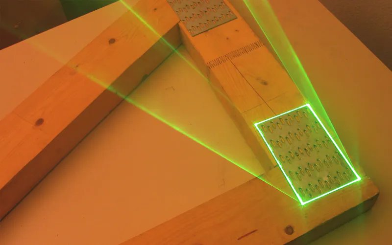 A green laser outline projected onto a timber truss joint, marking the exact position and size of the nail plate
