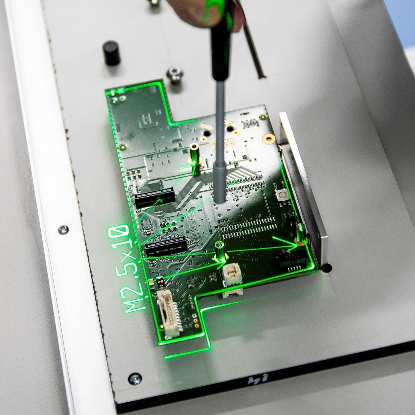 A circuit board on a mounting plate with its outline, fixing points and the screw size projected onto the plate in green laser
